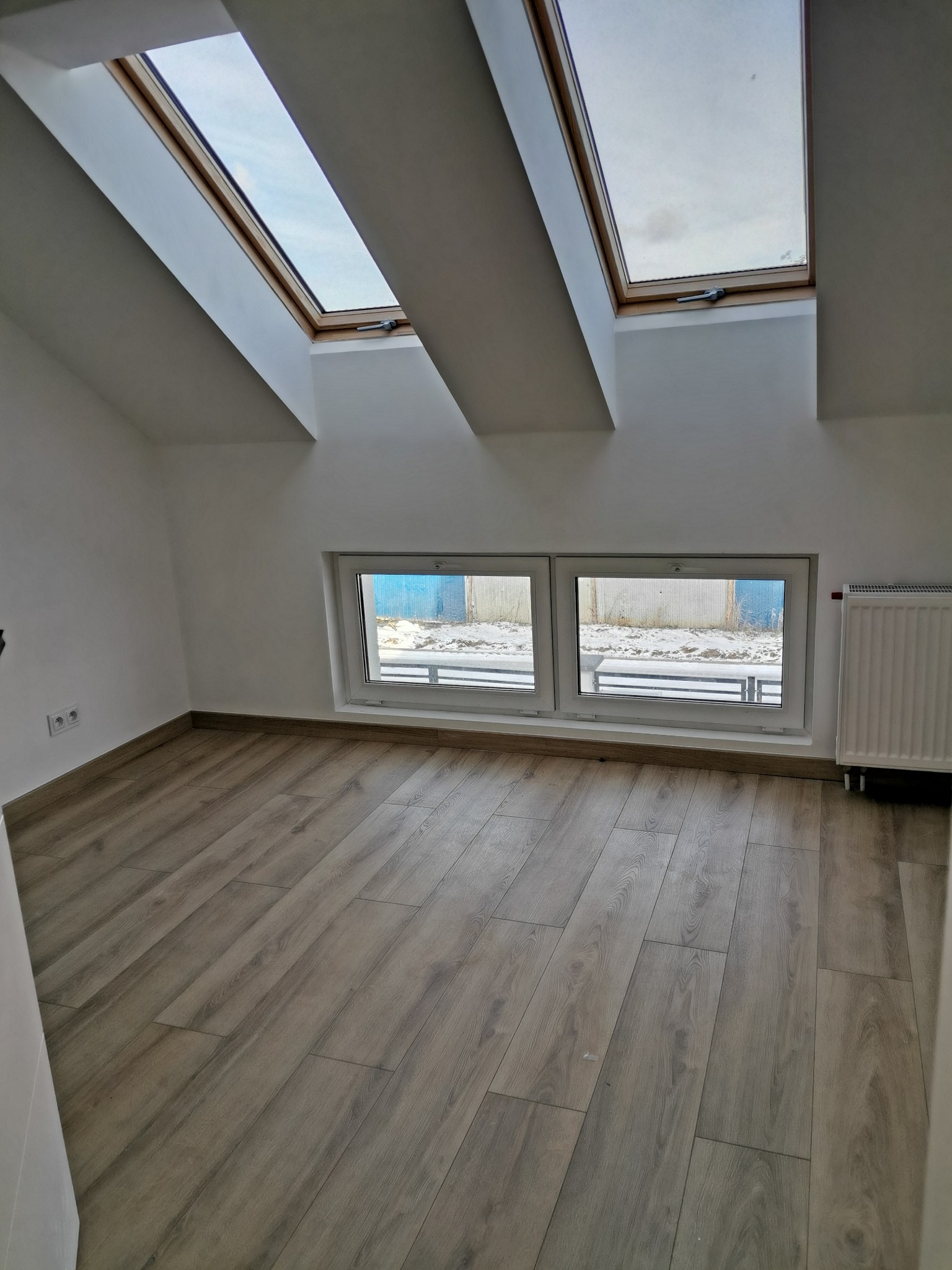Poddasze z drewnopodobną podłogą, dwoma oknami dachowymi i grzejnikiem, świeżo po remoncie.