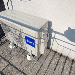 Makowski Group Energy - Zamontowana jednostka zewnętrzna klimatyzacji Haier na balkonie w Lublinie. Widoczne mocowania i cień barierki. Ściana budynku w tle.