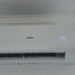 Makowski Group Energy - Biały klimatyzator Heiko z wyświetlaczem temperatury 14 stopni Celsjusza, zamontowany na białej ścianie w pomieszczeniu z oknem.