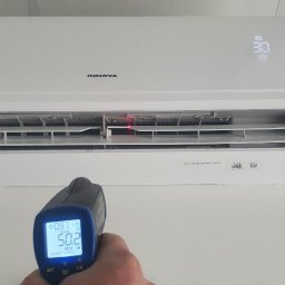 Makowski Group Energy - Biała klimatyzacja Innova na ścianie, sprawdzana termometrem laserowym. Wyświetlacz klimatyzacji pokazuje 30 stopni Celsjusza. Pomiar temperatury powietrza.