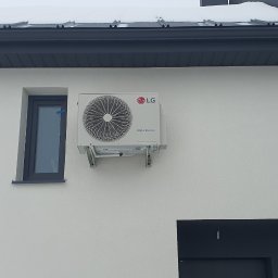 Makowski Group Energy - Biała elewacja domu z zamontowaną jednostką zewnętrzną klimatyzacji LG Dual Inverter, obok okno z ciemną ramą. Na dachu widoczny śnieg.