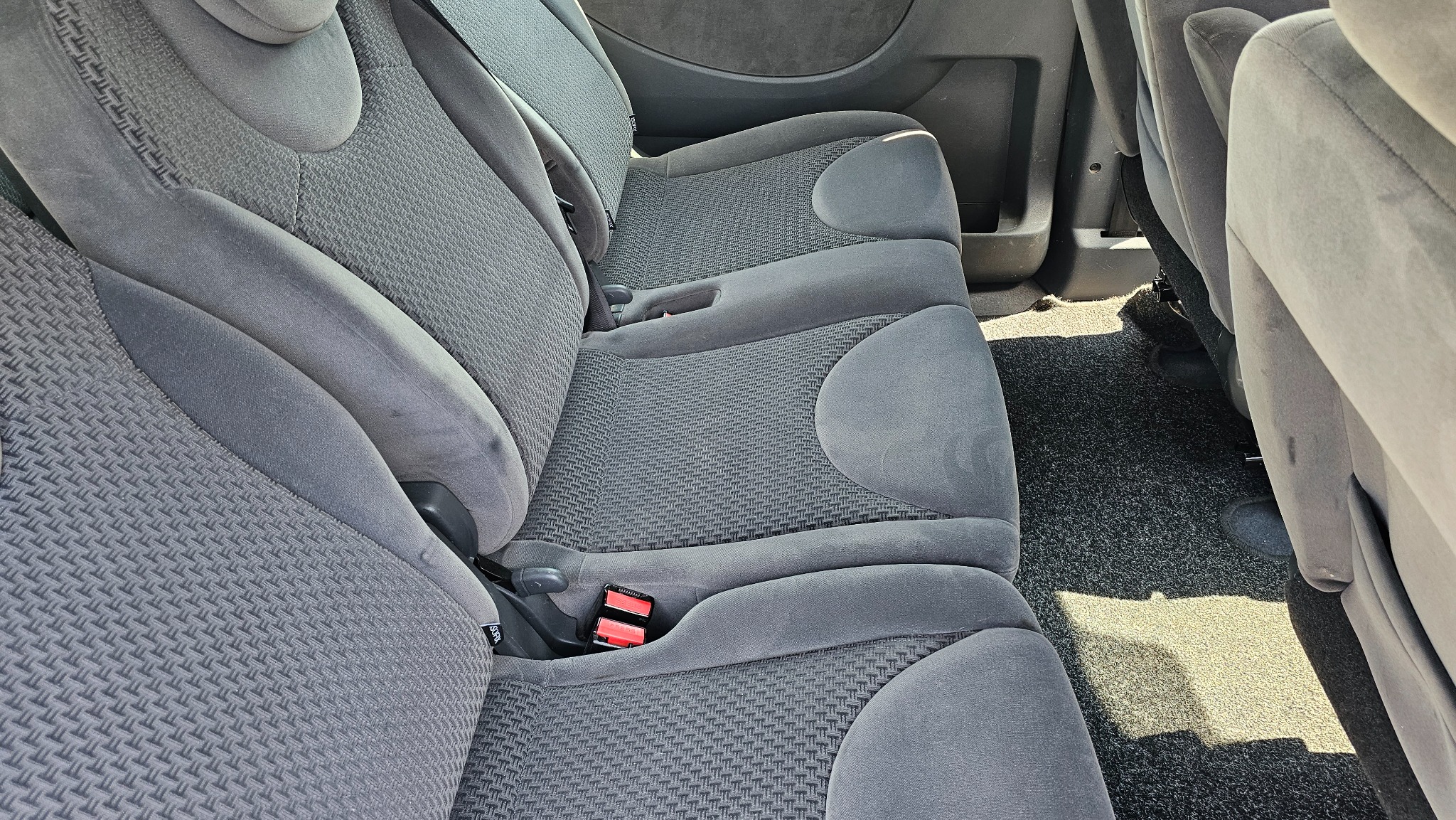 Szare, tekstylne siedzenia w samochodzie typu minivan, widok z góry, zapięty pas bezpieczeństwa na jednym z siedzeń.