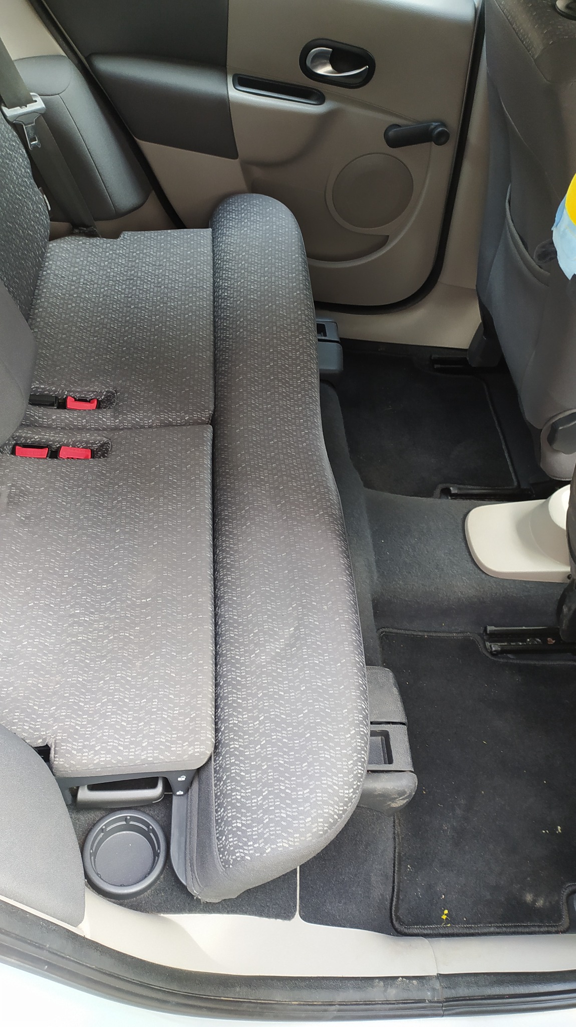 Wnętrze samochodu z widoczną tylną kanapą z szarej tapicerki o drobnym wzorze, czarną podłogą i elementami drzwi w odcieniach szarości.