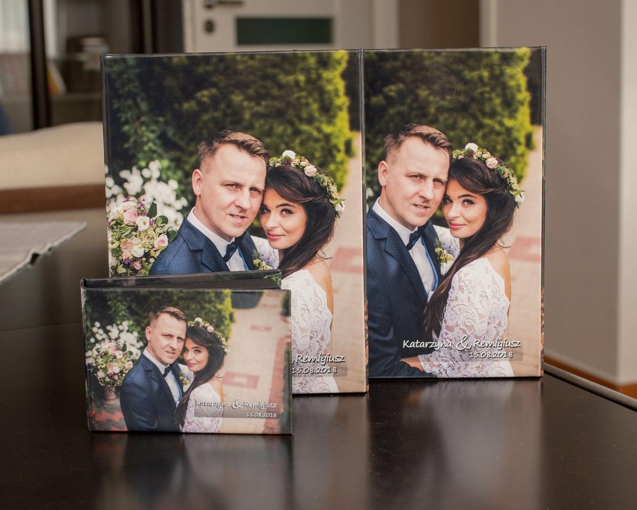 Trzy płótna z fotografią ślubną pary młodej, z datą 15.08.2018, ustawione na ciemnym blacie, w tle widoczne elementy wnętrza.