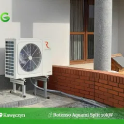 Zewnętrzna jednostka pompy ciepła Rotenso Aquami Split 10kW zamontowana na metalowej konstrukcji przy ścianie budynku z ceglanym cokołem i widocznymi oknami.