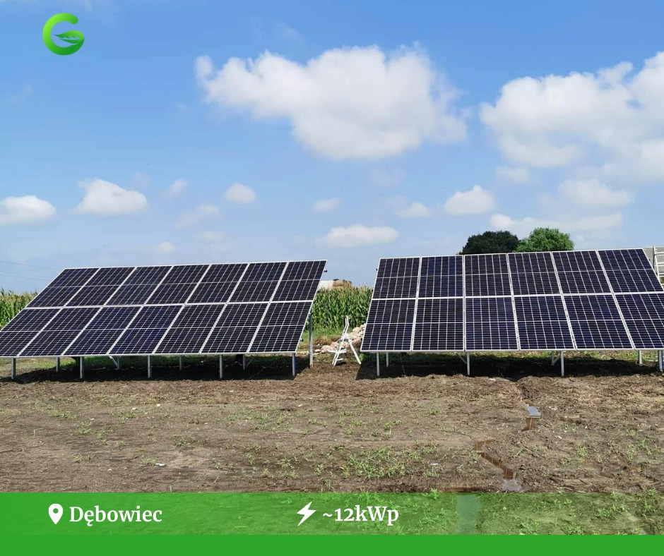 Dwa rzędy paneli słonecznych na metalowych konstrukcjach, ustawione na polu z młodą kukurydzą w tle, pod błękitnym niebem z białymi chmurami.