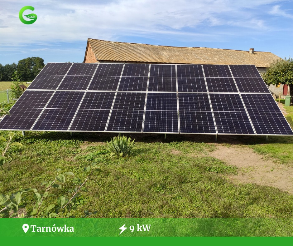 Panel słoneczny o mocy 9kW na trawiastym terenie, z widocznym budynkiem gospodarczym w tle i niebieskim niebem.