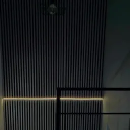 Ściana wykończona panelami pionowymi w kolorze czarnym i szarym z podświetleniem LED, widoczna lampa wisząca w stylu industrialnym i fragment schodów.