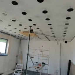 Przygotowanie do montażu sufitu podwieszanego: widoczne rozmieszczone uchwyty montażowe na suficie, rusztowanie i materiały budowlane w surowym wnętrzu.