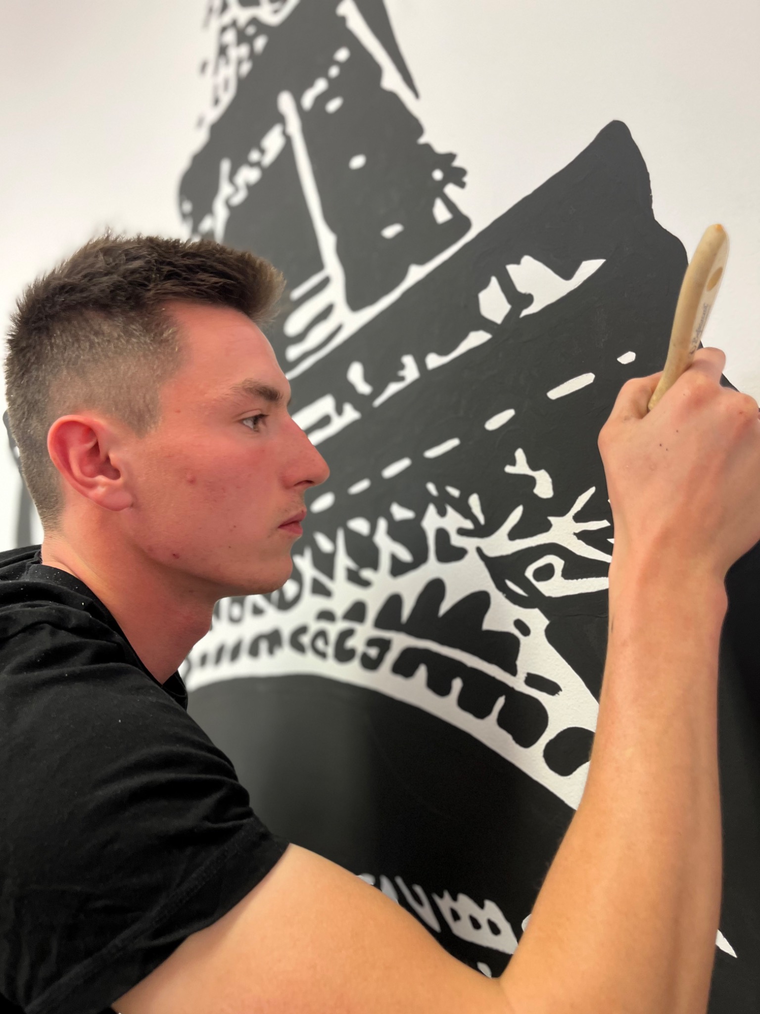 Artysta z Rudy Śląskiej maluje czarno-biały abstrakcyjny wzór na ścianie za pomocą pędzla.