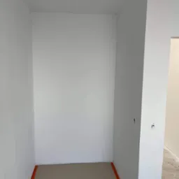 Pusta, świeżo pomalowana na biało przestrzeń z zabezpieczoną podłogą, widoczne ślady po pracach wykończeniowych i wystający kabel z sufitu.