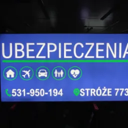 Podświetlany szyld reklamowy firmy ubezpieczeniowej z Nawojowej, z numerem telefonu, adresem i symbolami domu, samolotu, samochodu, rodziny i serca.