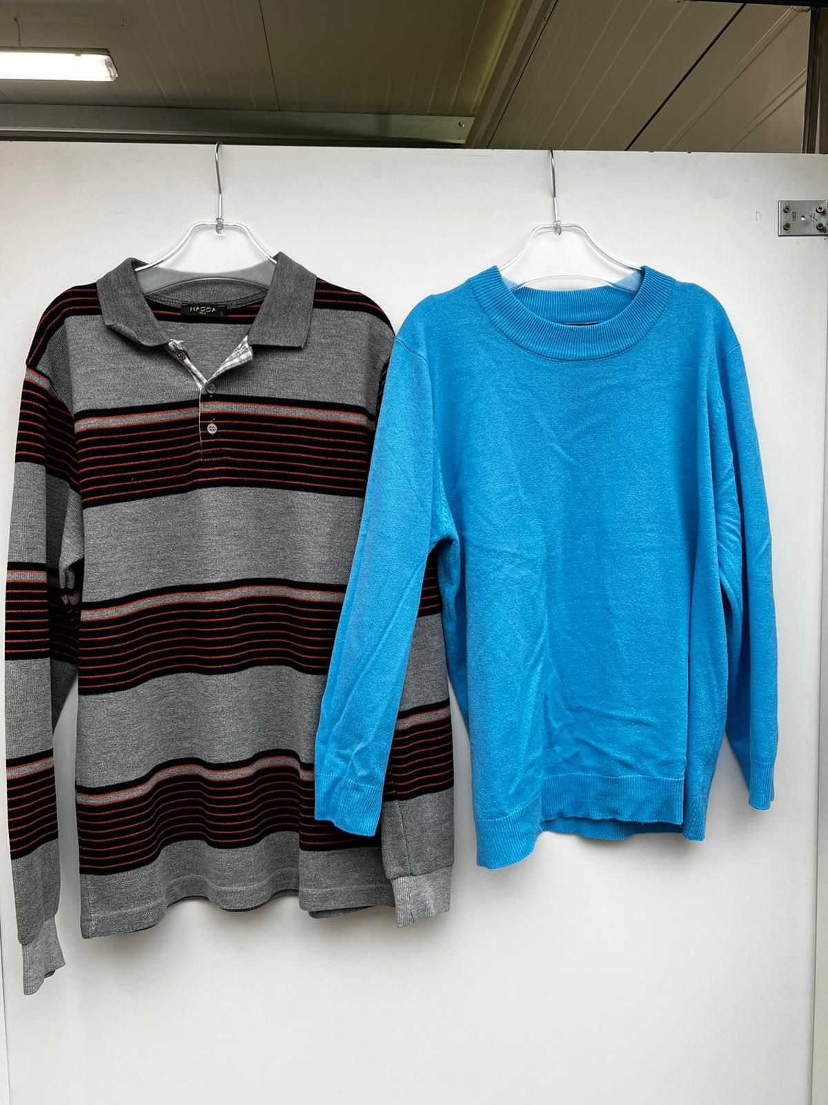 Dwa swetry wiszące na wieszakach: szary w paski z długim rękawem i kołnierzykiem polo oraz błękitny sweter z okrągłym dekoltem.