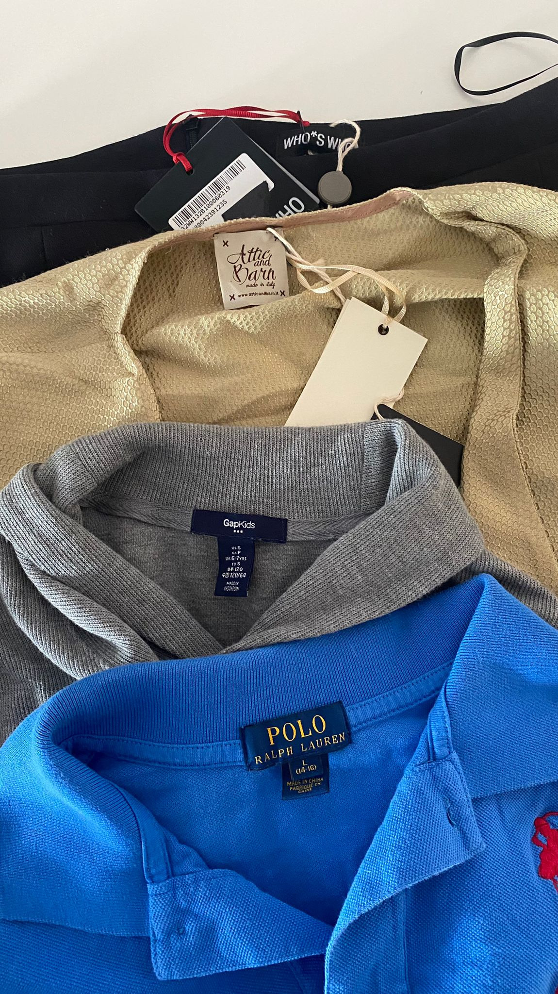 Stos ubrań: czarne spodnie z metką Who*s Who, złota bluzka Attic and Barn, szara bluza GapKids, niebieska koszulka polo Ralph Lauren z czerwonym logo gracza polo.