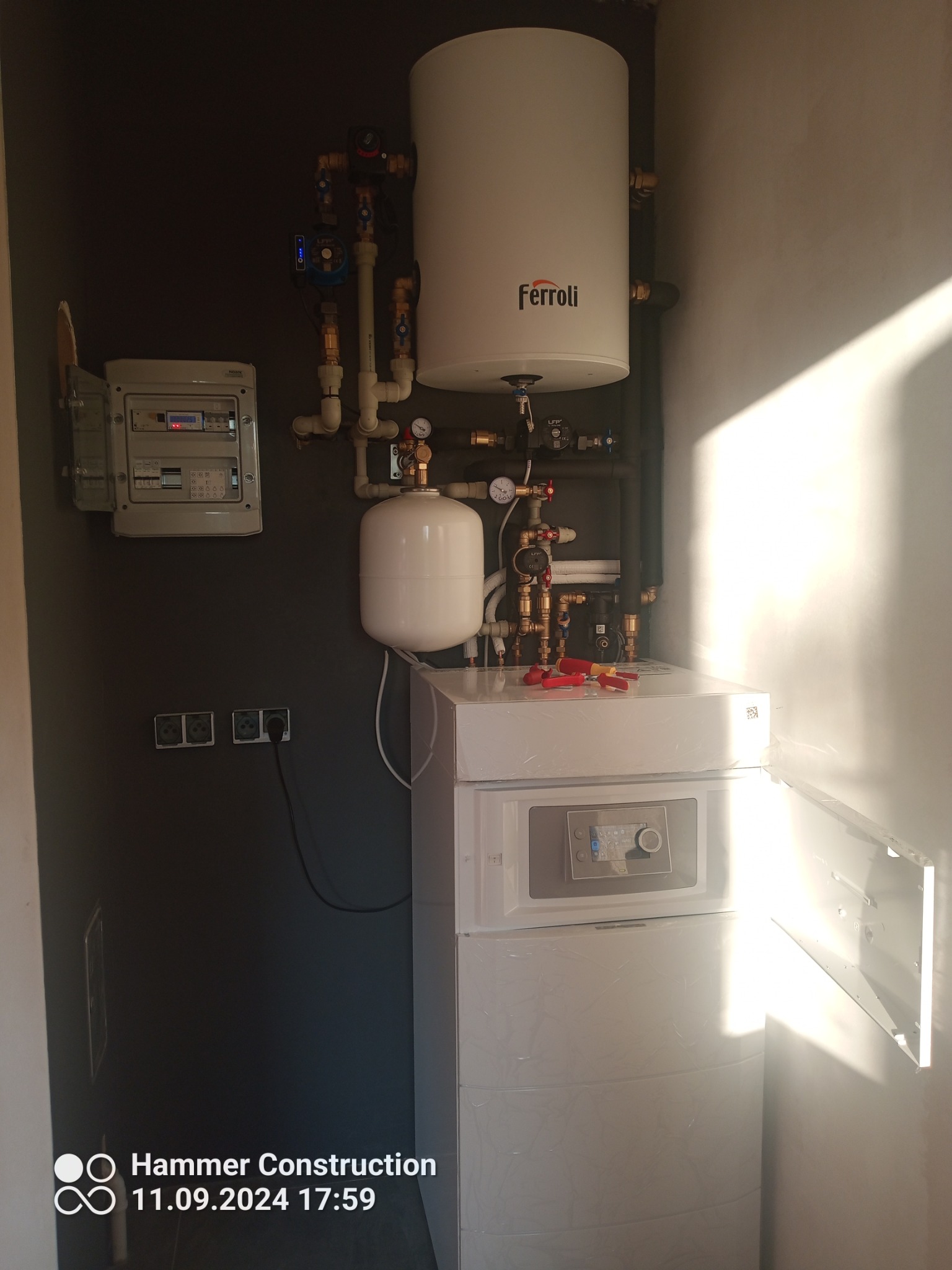 Nowoczesny piec gazowy Ferroli z podłączoną instalacją, widoczna szafka elektryczna, instalacja z zaworami i manometrami oraz narzędzia na górze pieca.