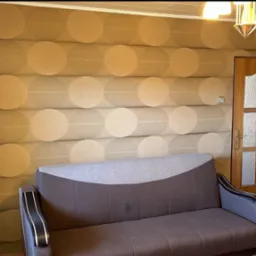 Wnętrze pokoju z brązową sofą na tle ściany pokrytej tapetą z geometrycznym wzorem w odcieniach beżu i brązu, obok drewniane drzwi z przeszkleniami.