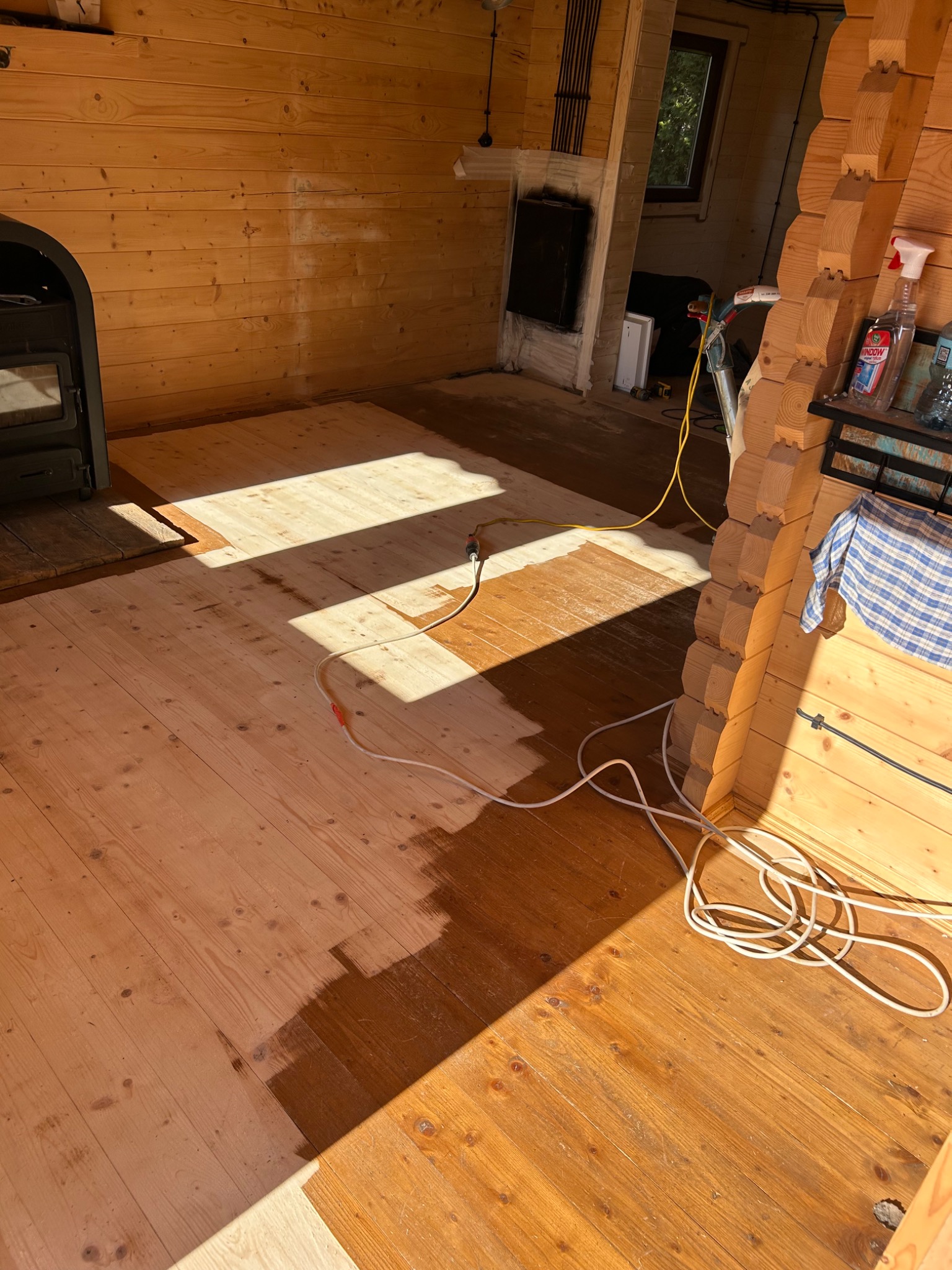 Częściowo wykończona drewniana podłoga z widocznymi śladami szlifowania i lakierowania w domu w Częstochowie, z widocznym sprzętem i kablami.