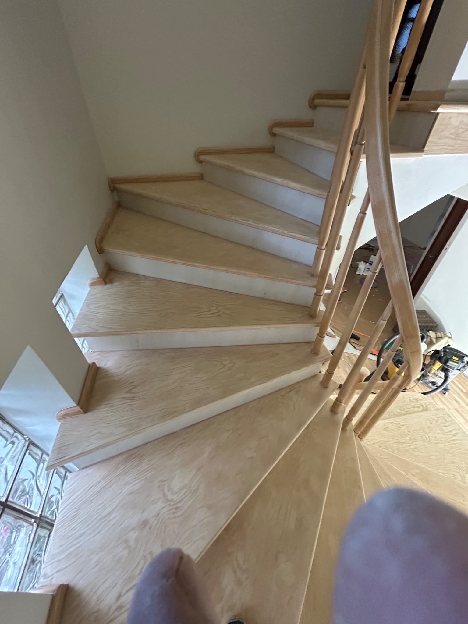 Jasne, drewniane schody spiralne z balustradą, widok z góry. Widoczne narzędzia i materiały budowlane w tle. Naturalne oświetlenie podkreśla strukturę drewna.