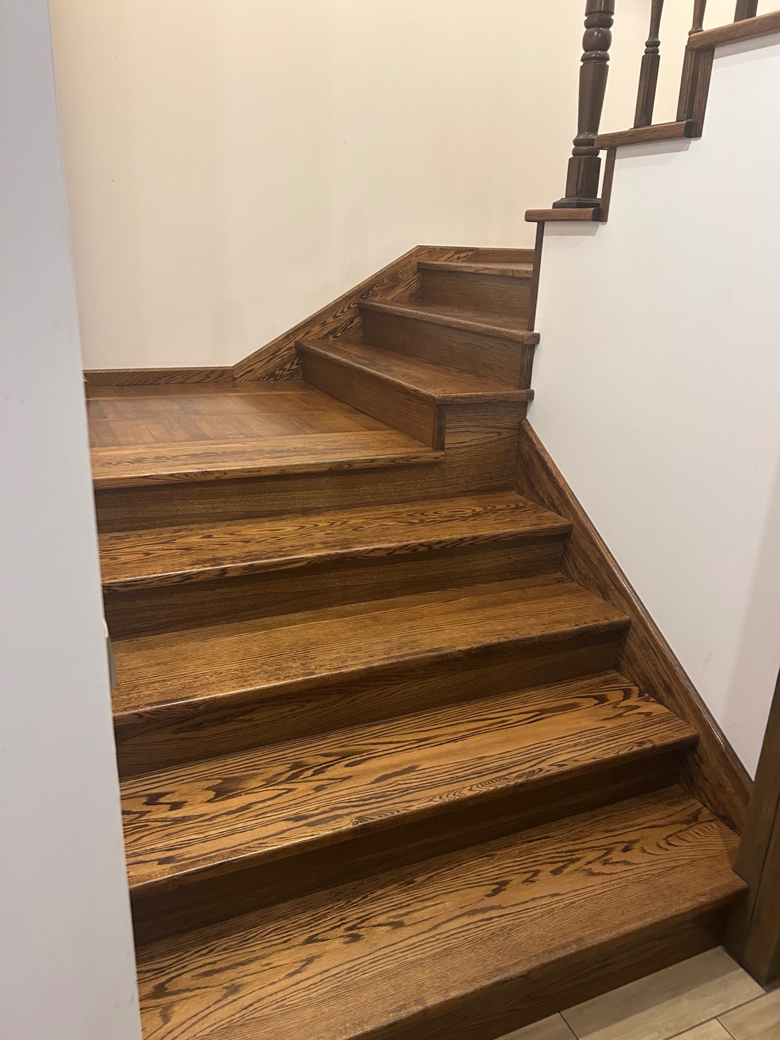 Odnowione drewniane schody z ciemnym bejcowaniem, widoczne słoje drewna. Ujęcie z dołu, ukazujące detale wykończenia i kontrast z białą ścianą.