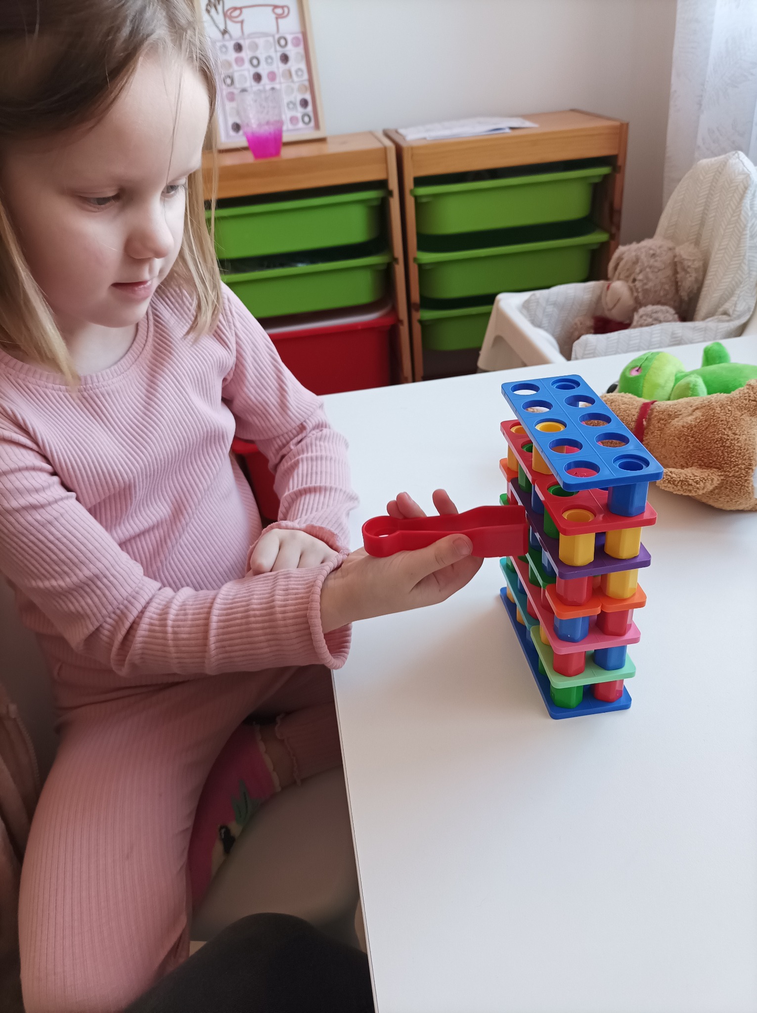 Dziewczynka w Rybniku skupiona na ćwiczeniu motoryki małej, używając kolorowej wieży z otworami i szczypiec.