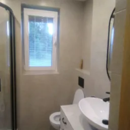 Jasna łazienka po remoncie z kabiną prysznicową, umywalką nablatową na szafce z szufladami i toaletą w zabudowie, wykończona beżowymi płytkami.