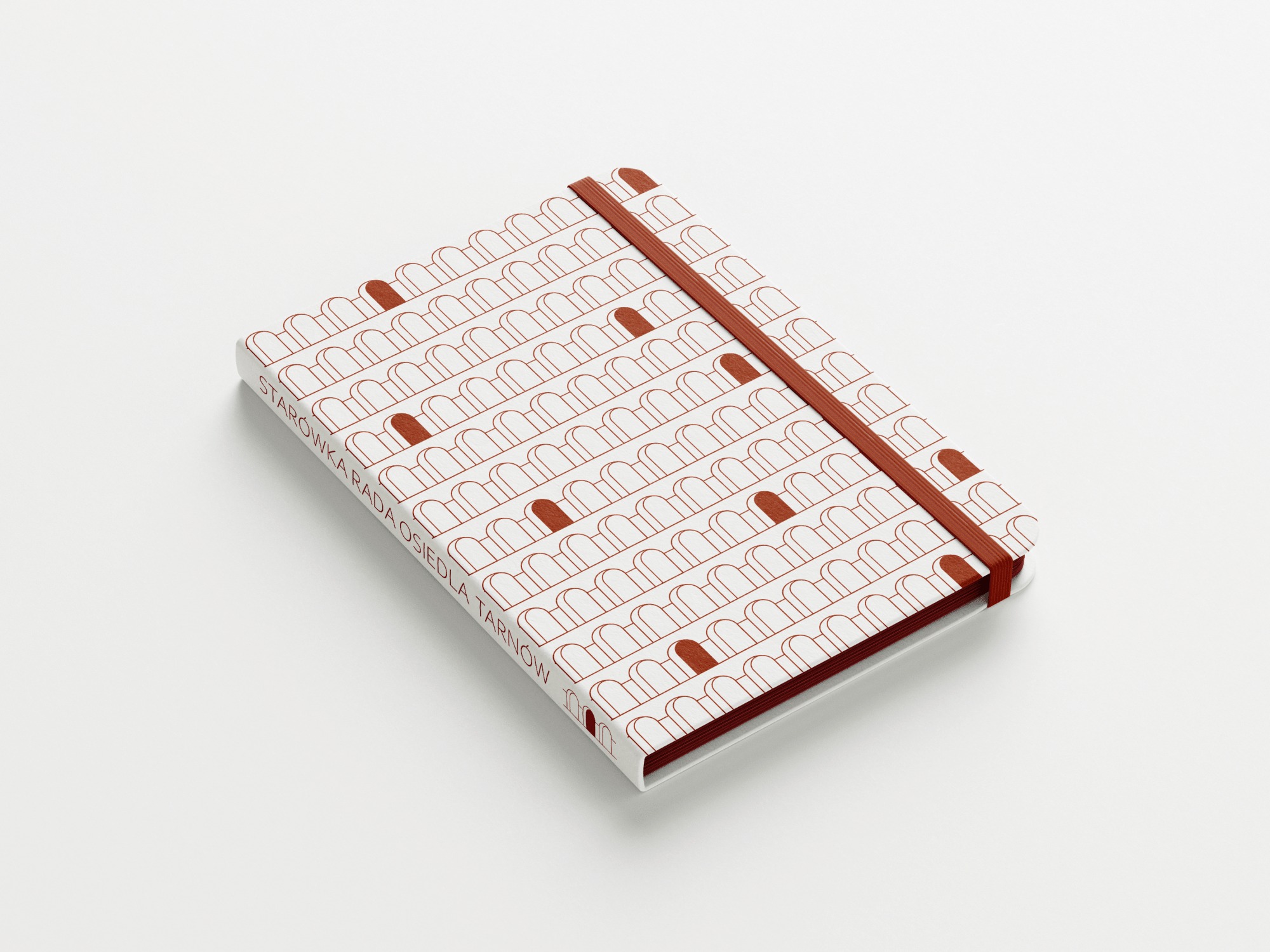 Zamknięty notatnik z brązowymi detalami graficznymi i gumką, leżący na białym tle, z napisem 'STAROWKARADA OSIEDLA TARNOW'