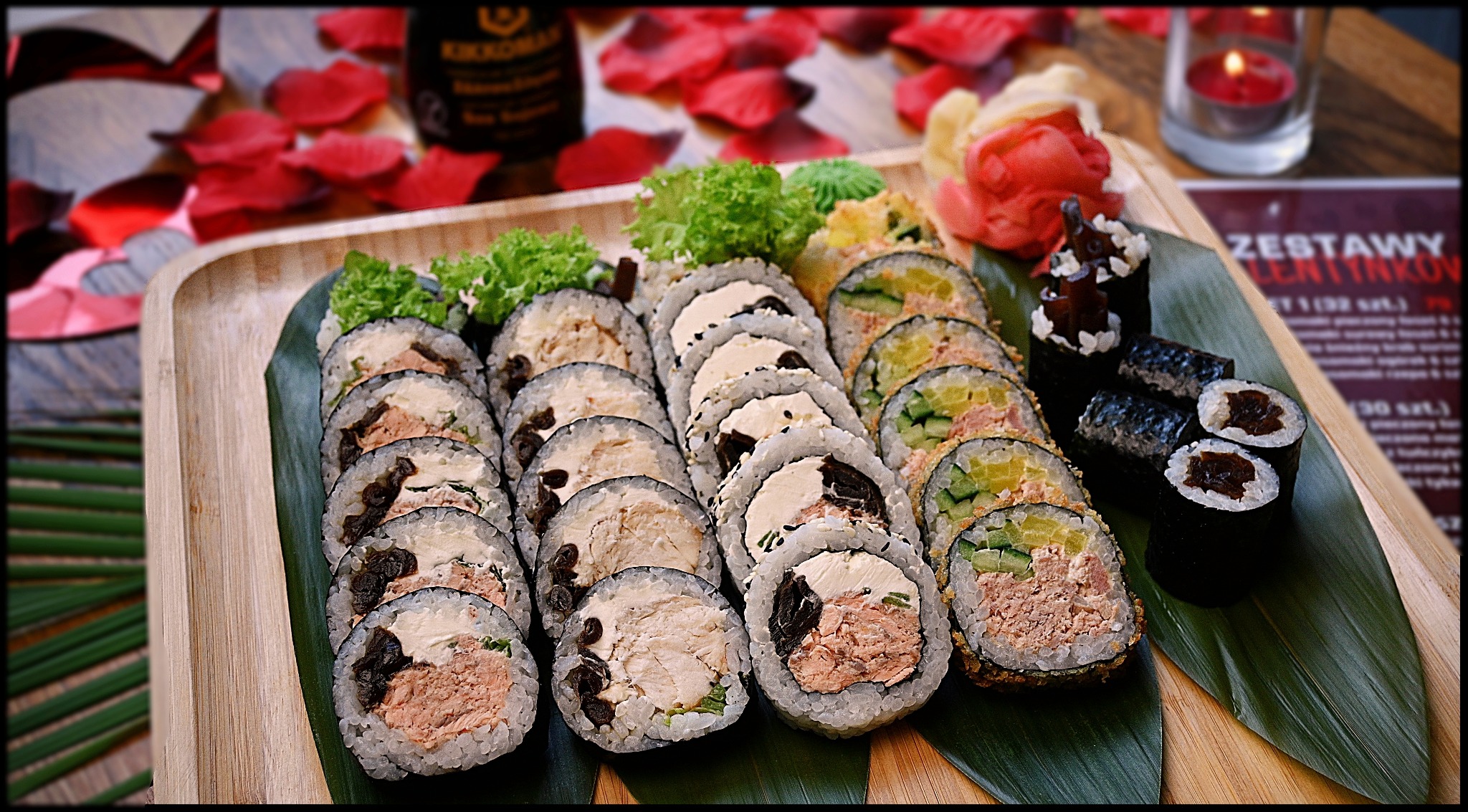 Zestaw sushi na drewnianej tacy z liściem, dekorowany płatkami róż, sosem sojowym i świecą, w tle menu walentynkowe.