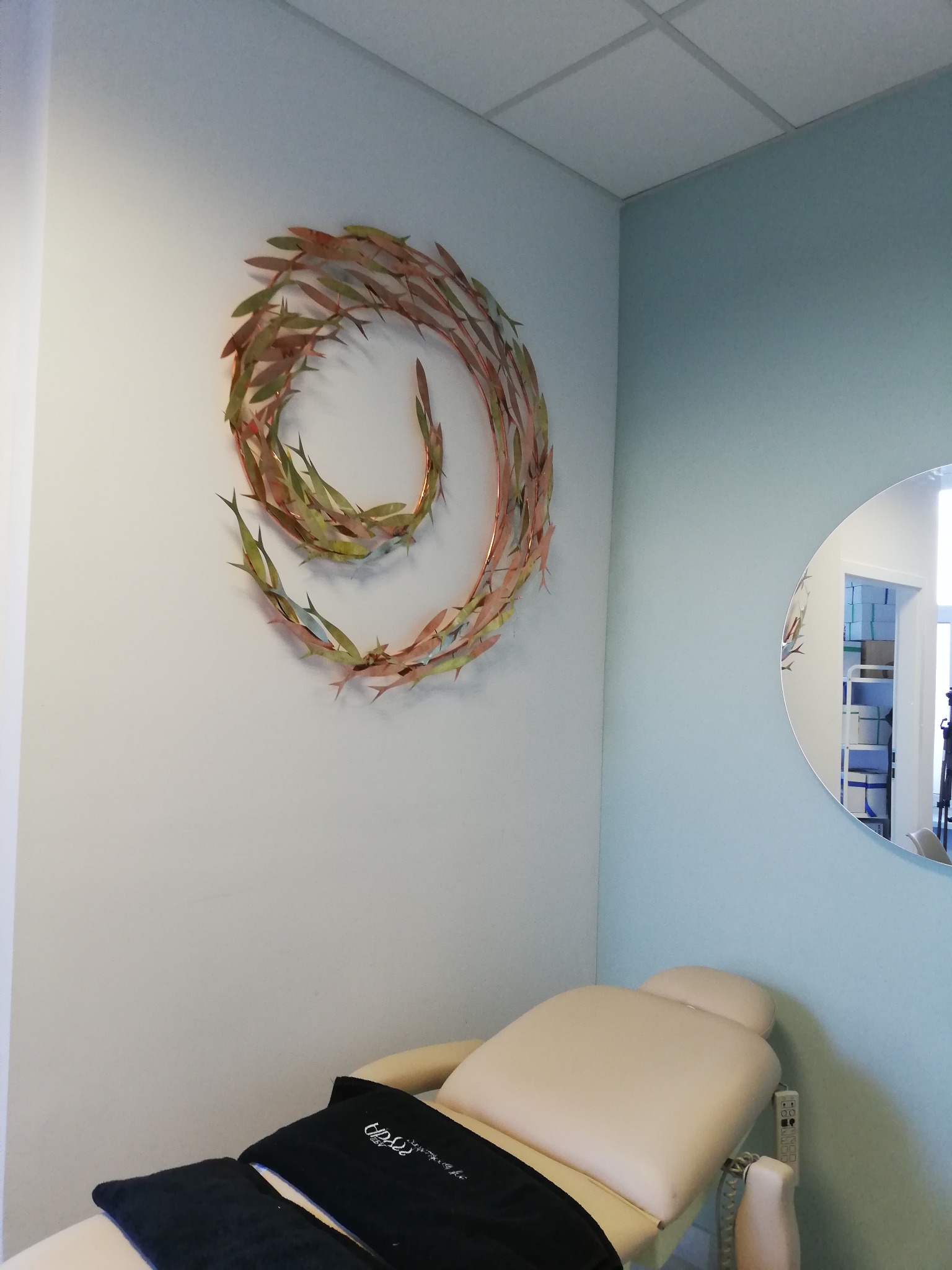 Gabinet kosmetyczny z metalową dekoracją ścienną w kształcie stada ryb i beżowym fotelem do zabiegów.