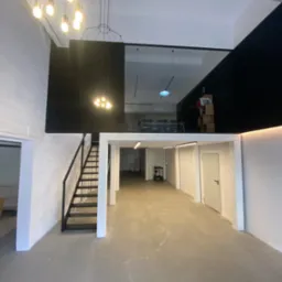 Wnętrze hali produkcyjnej z antresolą, czarne schody metalowe prowadzące na górę, widoczne oświetlenie i wykończenie ścian.