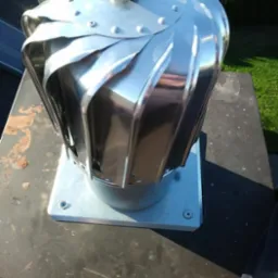 Błyszcząca, metalowa nasada kominowa typu turbowent z czarną kulką na szczycie, zamontowana na kominie, widok z góry pod kątem.