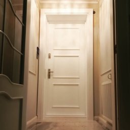 Artur Grela ELart Design - Białe drzwi wewnętrzne z trzema prostokątnymi panelami, widoczne z perspektywy korytarza z marmurową podłogą i dekoracyjnymi listwami ściennymi.