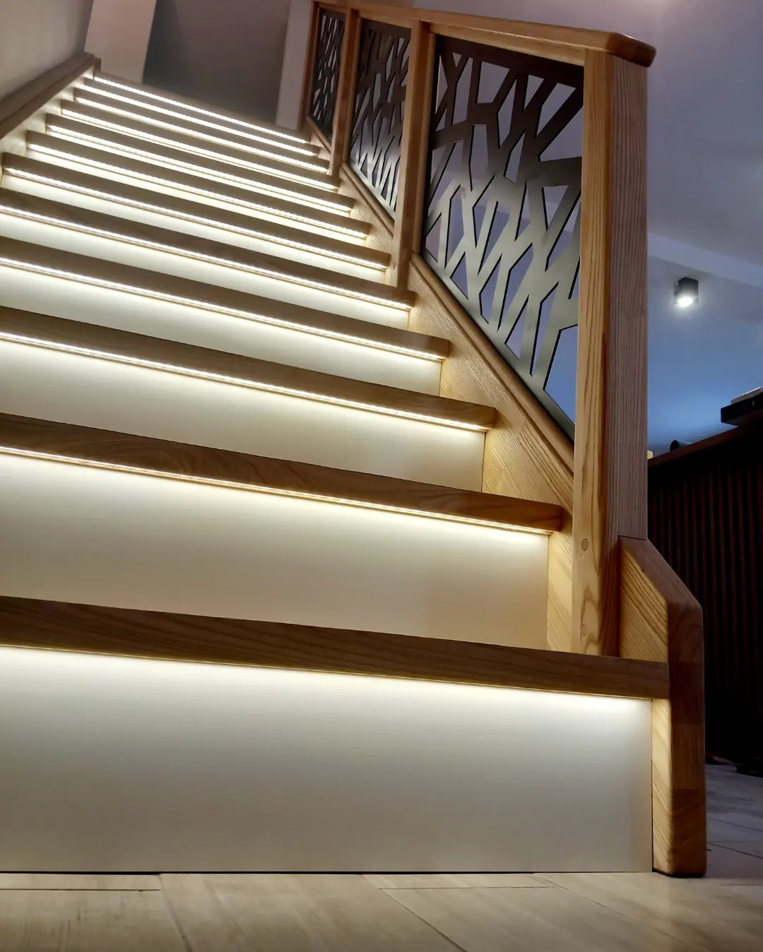 Nowoczesne schody w Sobolewie z podświetleniem LED pod każdym stopniem i ażurową balustradą z ciemnego metalu, widok z dołu.