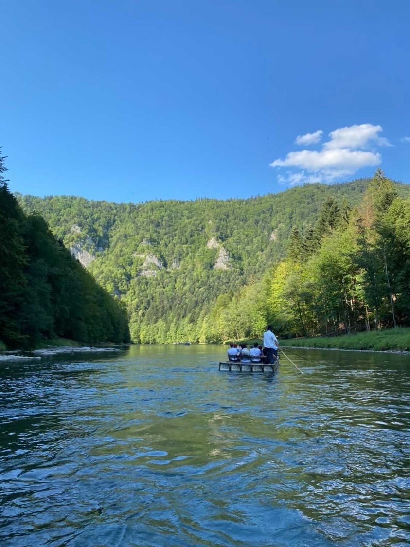 Spokojny spływ tratwą po rzece otoczonej zielonymi wzgórzami w słoneczny dzień.