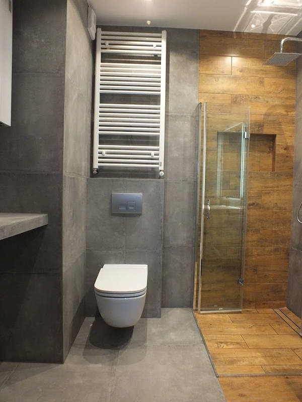 Nowoczesna łazienka z szarymi płytkami, podwieszaną toaletą, grzejnikiem drabinkowym i kabiną prysznicową z drewnopodobnymi płytkami.