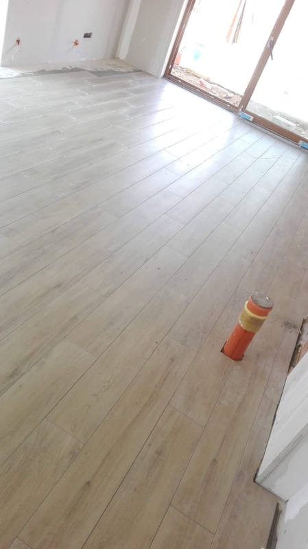 Ułożona podłoga z paneli imitujących drewno w jasnym odcieniu, z widoczną rurą wystającą z podłoża i fragmentem ściany w trakcie prac wykończeniowych.