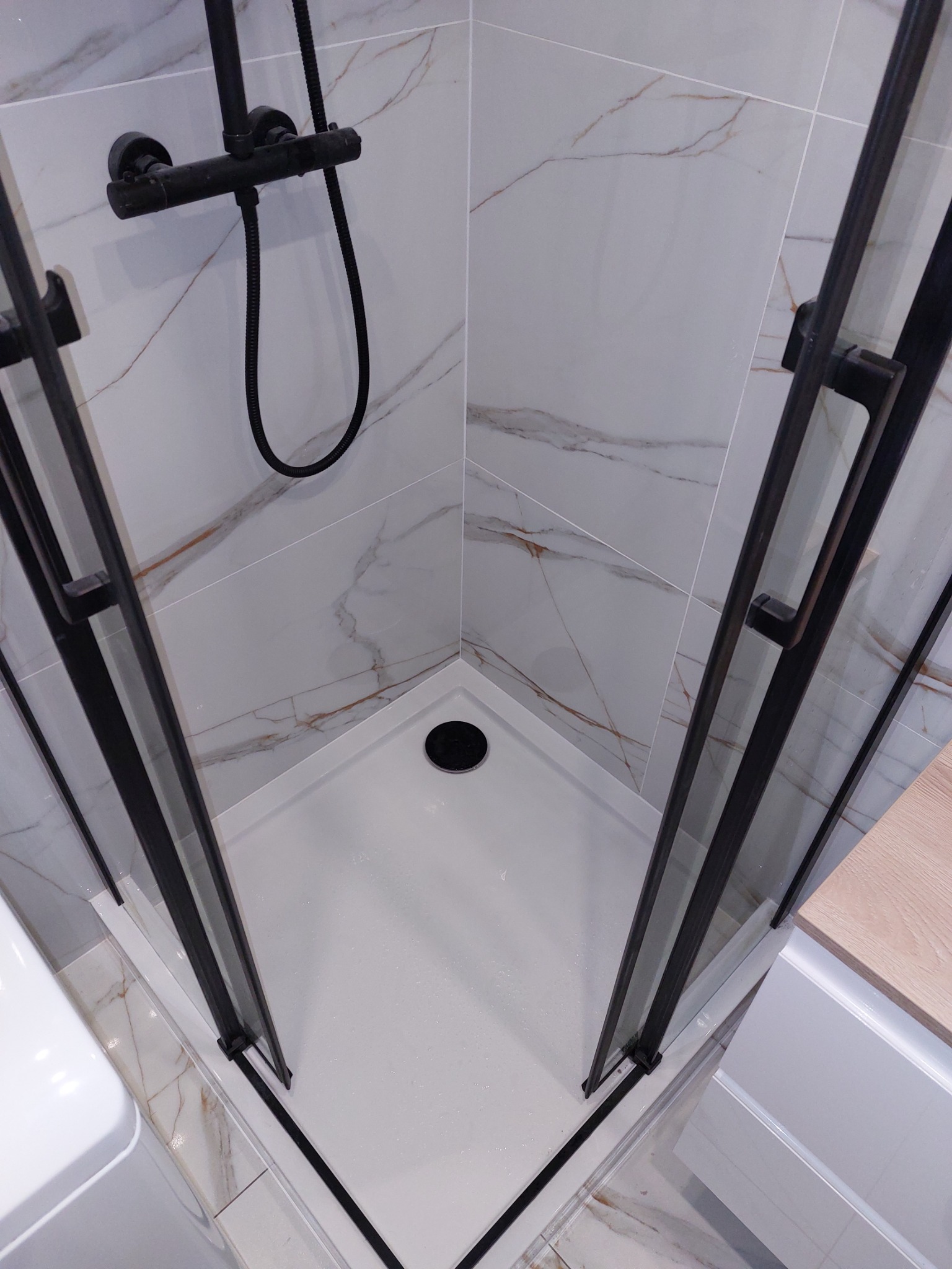 Nowoczesna kabina prysznicowa z czarnymi profilami i armaturą na tle marmurowych płytek.