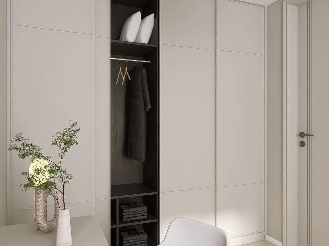 Wnętrze garderoby z minimalistycznym designem: beżowe szafy z panelami, otwarty regał z ubraniami i poduszkami, dekoracyjna lampa w wazonie na blacie.