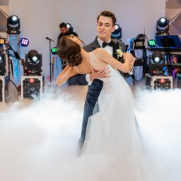 Hocus-Pocus.pl - Wesela i Eventy - Para młoda tańczy pierwszy taniec w chmurze dymu na tle sceny z oświetleniem i zespołem muzycznym.