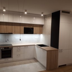 TARAS-MEB Michał Pawlik - Nowoczesna kuchnia w odcieniach bieli i drewna, z jasnymi frontami szafek górnych i dolnych, drewnianymi blatami i czarnymi akcentami w postaci piekarnika, płyty indukcyjnej i wnęki na wino...