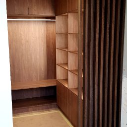 TARAS-MEB Michał Pawlik - Wnętrze garderoby z drewnianymi szafkami, półkami i wbudowanym oświetleniem LED, oddzielone od reszty pomieszczenia ażurową ścianką działową; podłoga zabezpieczona kartonem.