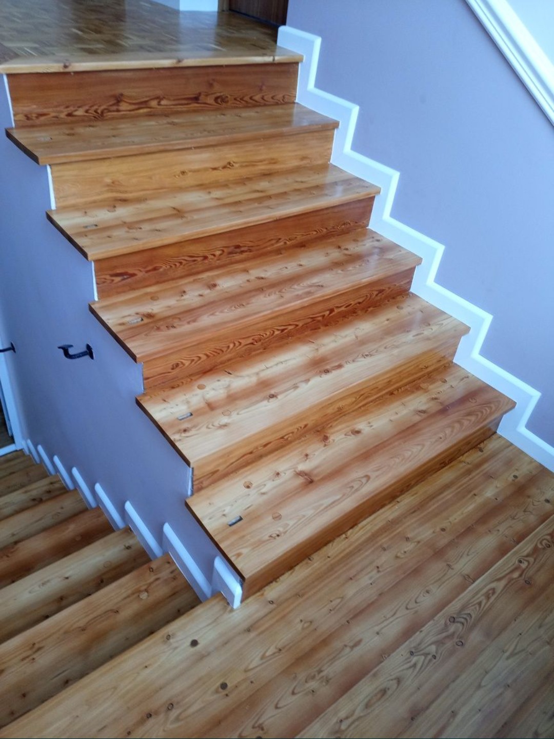 Odnowione drewniane schody z widocznym rysunkiem słojów, pomalowane ściany i listwy przypodłogowe.