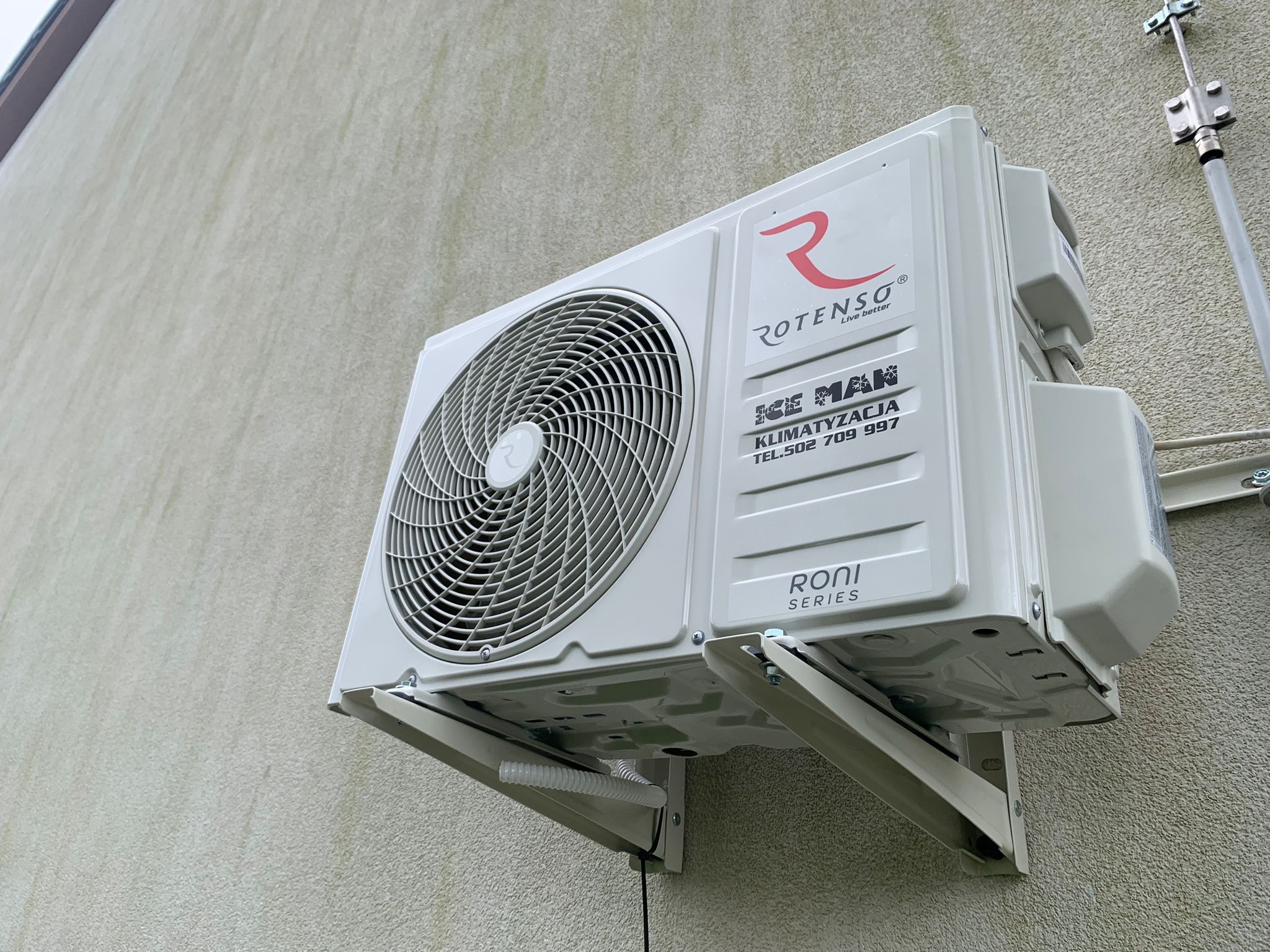 Zamontowana na zewnątrz jednostka klimatyzacji Rotenso Ice Man Roni Series na jasnej ścianie budynku, widoczne mocowania i przewody.
