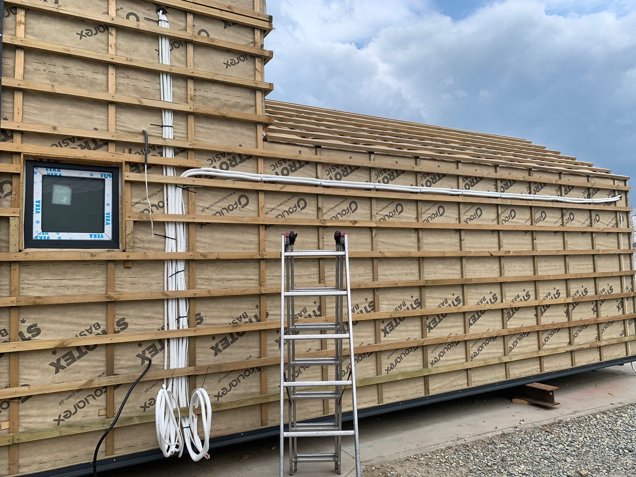 Montaż instalacji na elewacji budynku w trakcie budowy, widoczne przewody, drabina oparta o ścianę z oknem.