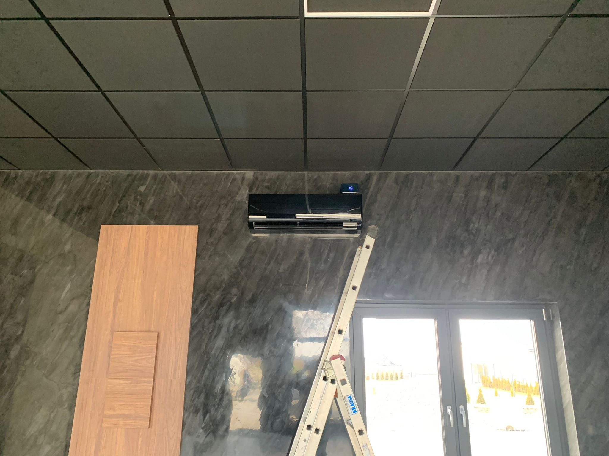 Czarna klimatyzacja na ścianie o teksturze marmuru w Czernicy, drabina oparta o ścianę, widoczne okno z widokiem na zewnątrz.