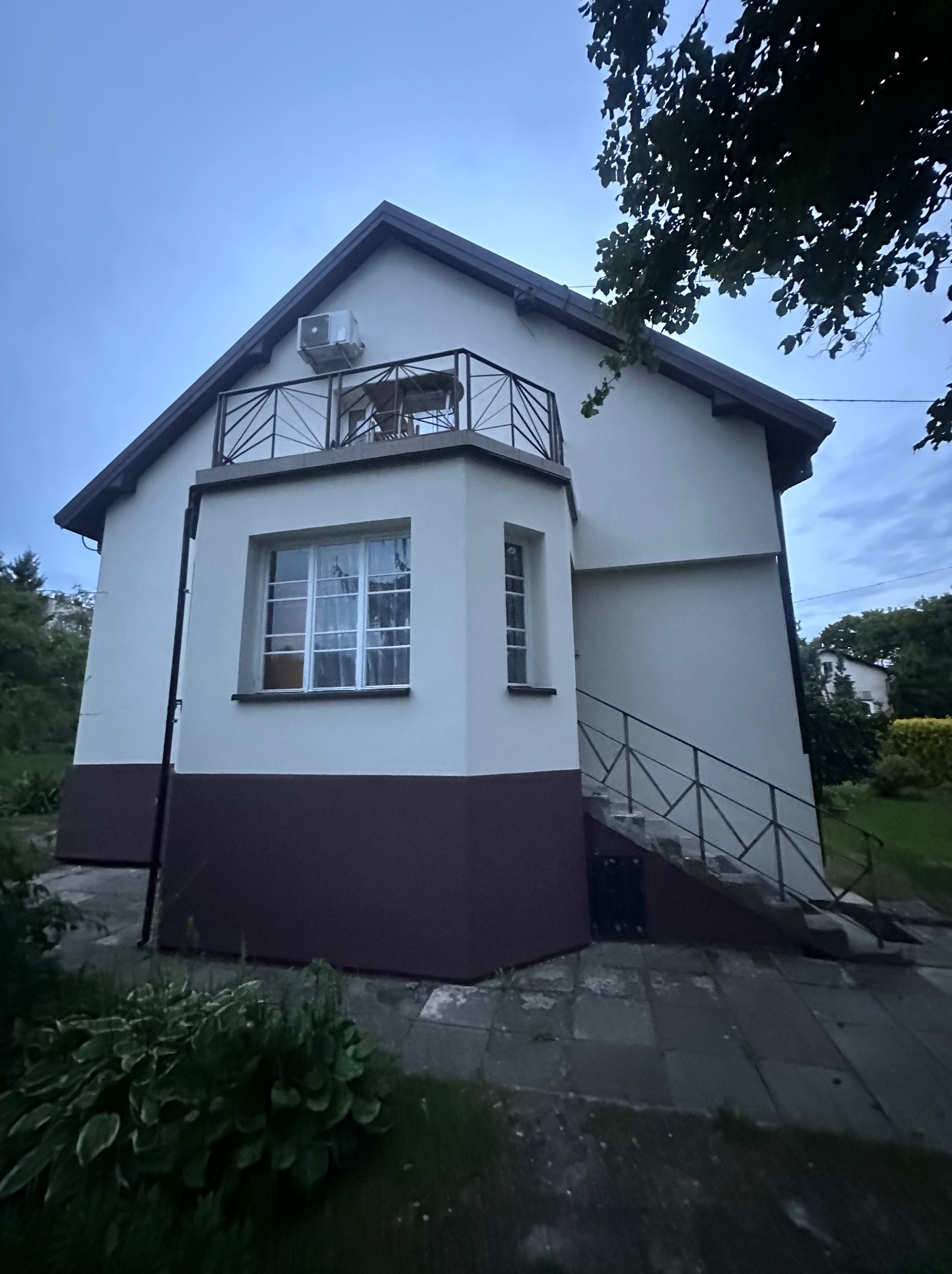 Dom jednorodzinny z balkonem i schodami zewnętrznymi, świeżo po renowacji elewacji w kolorach beżu i brązu, z widocznym klimatyzatorem na ścianie.