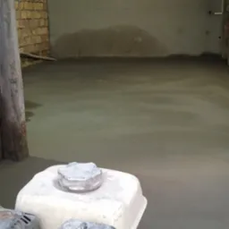 Świeżo wylana, mokra posadzka w pomieszczeniu z ceglaną ścianą, widoczna maszyna do zacierania posadzek z silnikiem spalinowym.