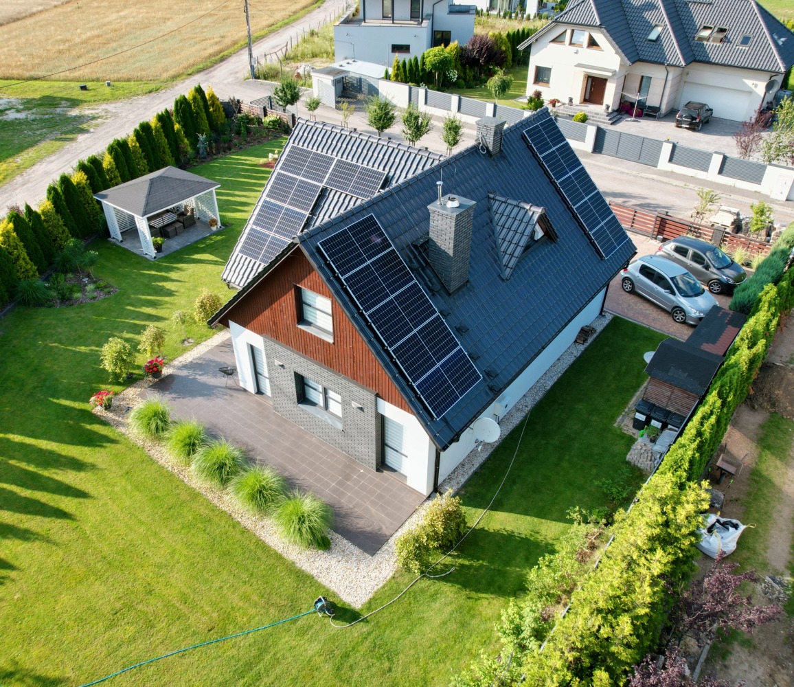 Dom jednorodzinny z zainstalowanymi panelami słonecznymi na dachu, widok z góry, zadbany ogród z altaną i dwoma samochodami zaparkowanymi obok