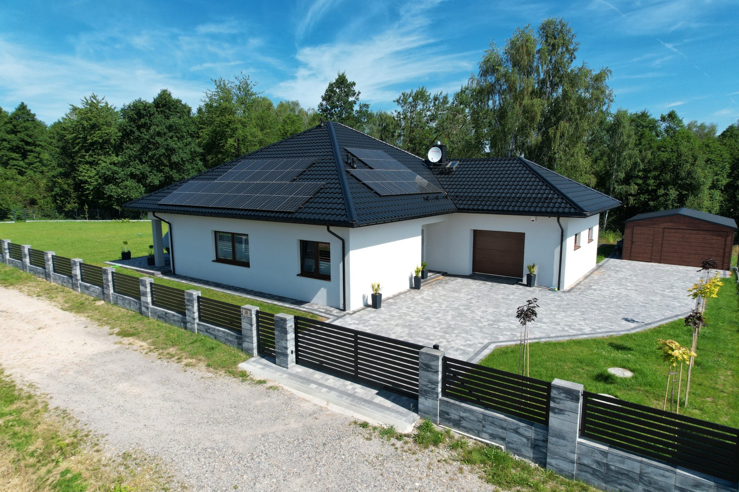 Nowoczesny dom jednorodzinny z czarną dachówką i panelami słonecznymi na dachu, widok z góry, ogrodzenie panelowe z elementami imitującymi kamień