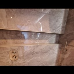 Dariusz Zambrzycki DMM Usługi Glazurnicze - Wykończona łazienka z marmurowymi płytkami, półkami i złotą armaturą. Widoczne detale wykończenia i nowoczesny design.