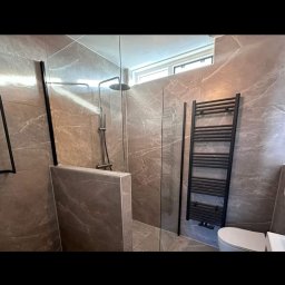 Dariusz Zambrzycki DMM Usługi Glazurnicze - Wykończona łazienka z kabiną prysznicową typu walk-in, grzejnikiem drabinkowym i toaletą. Płytki imitujące marmur na ścianach i podłodze. Czarny osprzęt.
